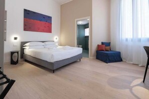 Ett modernt hotellrum med en säng, en liten sittgrupp och en tavla på väggen.