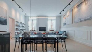 Ein moderner Essbereich mit Glastisch und Stühlen, einem Fernseher und einem Bücherregal.
