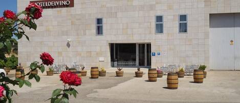 A building with a sign reading 'HOTELDELVINO,' a parking lot, and several potted plants and barrels.
