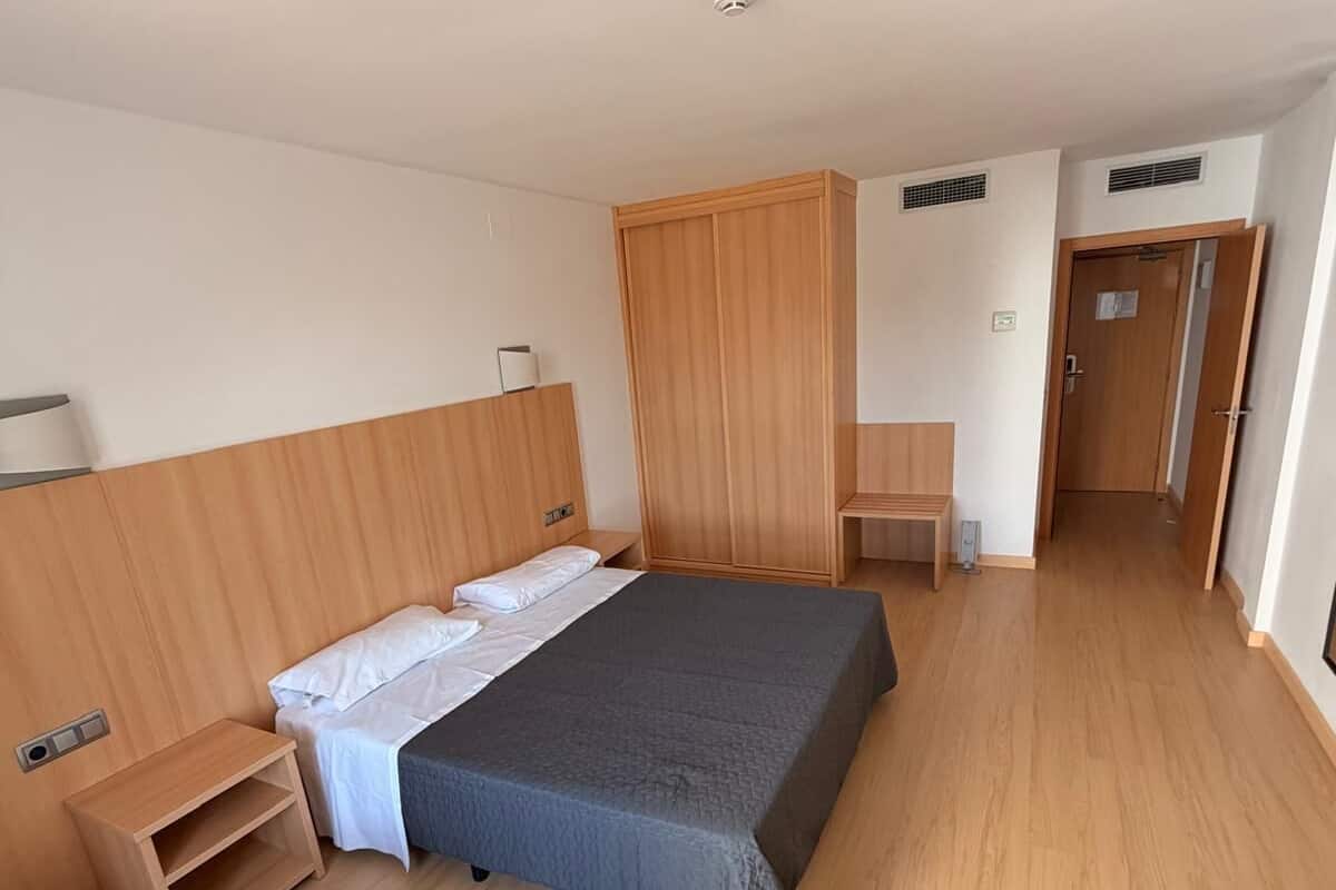 Un dormitorio con cama, mesita de noche, silla, armario y un escritorio pequeño.