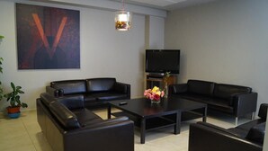 Uma sala de estar moderna com dois sofás de couro preto, uma mesa de centro, uma TV de tela plana e um grande quadro abstrato na parede.