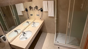 Casa de banho moderna com duas pias, espelho, secador de cabelo e cabine de duche em vidro.