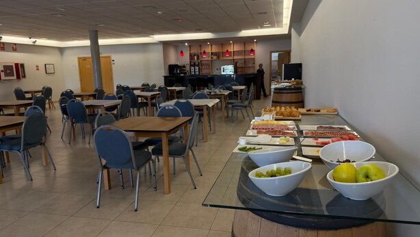 Uma cafeteria com mesas, cadeiras, um balcão de comida e uma tela de televisão.