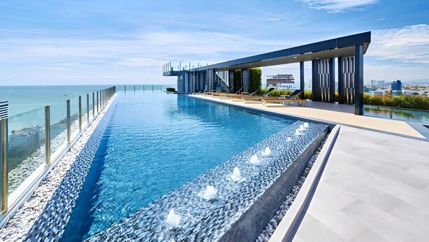 Ein moderner Infinity-Pool mit freiem Blick auf den Ozean, ein überdachter Außenbereich mit Liegestühlen und eine Stadtkulisse im Hintergrund.