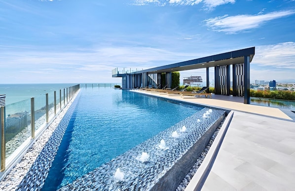 A modern infinity pool with a clear view of the ocean, a covered outdoor area with lounge chairs, and a cityscape in the background. - The Base Central Pattaya - Rooftop Pool (Muang Pattaya)