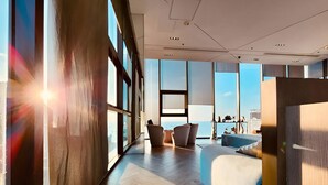 Ein modernes Hotelzimmer mit großen Fenstern, einem Bett, einer Sitzecke und Blick auf die Stadt.