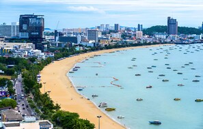 A coastal cityscape with a wide sandy beach, numerous boats, and a dense urban area in the background. - The Base Central Pattaya - Rooftop Pool (Muang Pattaya)