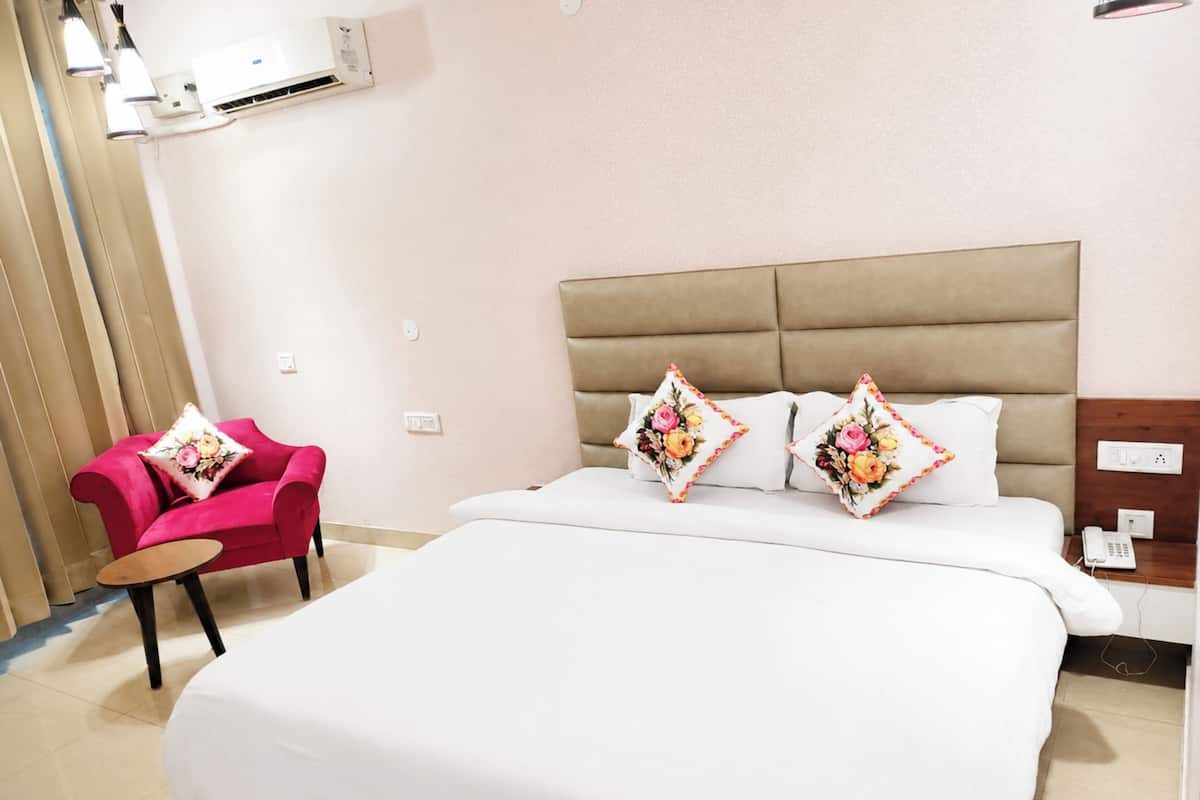 A hotel room with a bed, a chair, a bedside table, and an air conditioning unit.