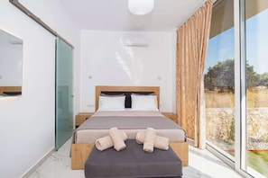A bedroom with a bed, a bedside table, a large window, and a view of the outdoors.