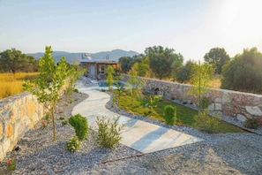 A landscaped outdoor area with a stone wall, a winding pathway, and a building with a sloped roof.