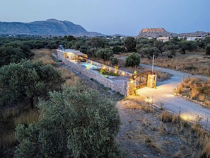 A stone-walled property with a pool, a covered seating area, and a view of distant mountains.