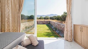 Una camera da letto con un'ampia porta scorrevole in vetro che dà su un giardino con muro in pietra e vista su colline lontane.