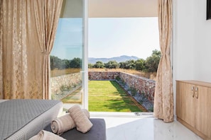 A bedroom with a large sliding glass door leading to a garden with a stone wall and a view of distant hills.