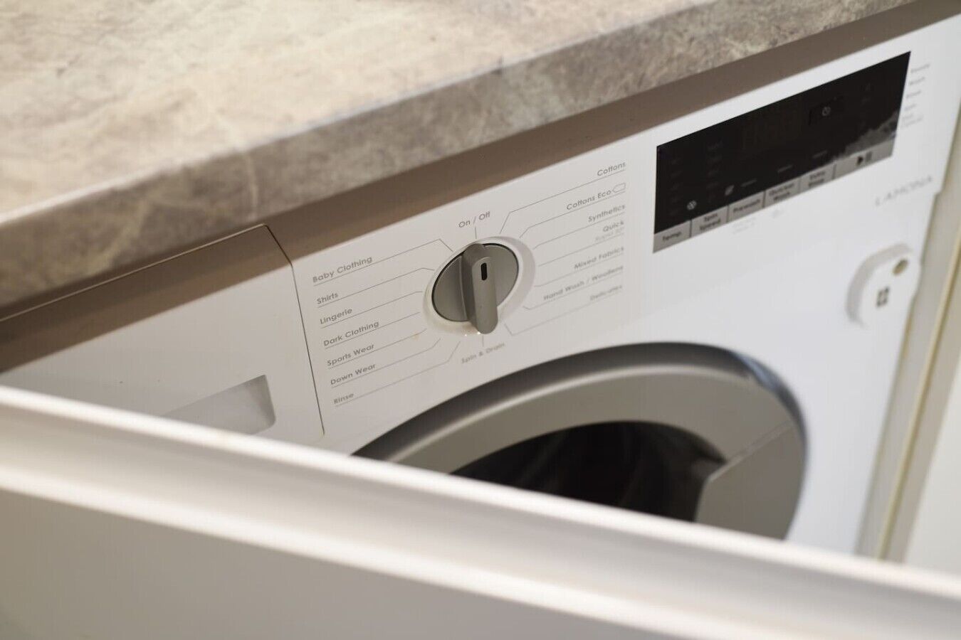 Een wasmachine met een bedieningspaneel waarop opties staan vermeld zoals babykleding, overhemden en sportkleding.