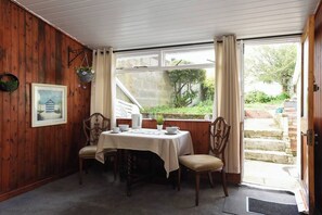 A room with a wooden interior, a table with chairs, a window with curtains, and a door leading outside. - Clarence Cottage | 4mins to Pier, Pet Friendly with Shared Garden (Portsmouth)