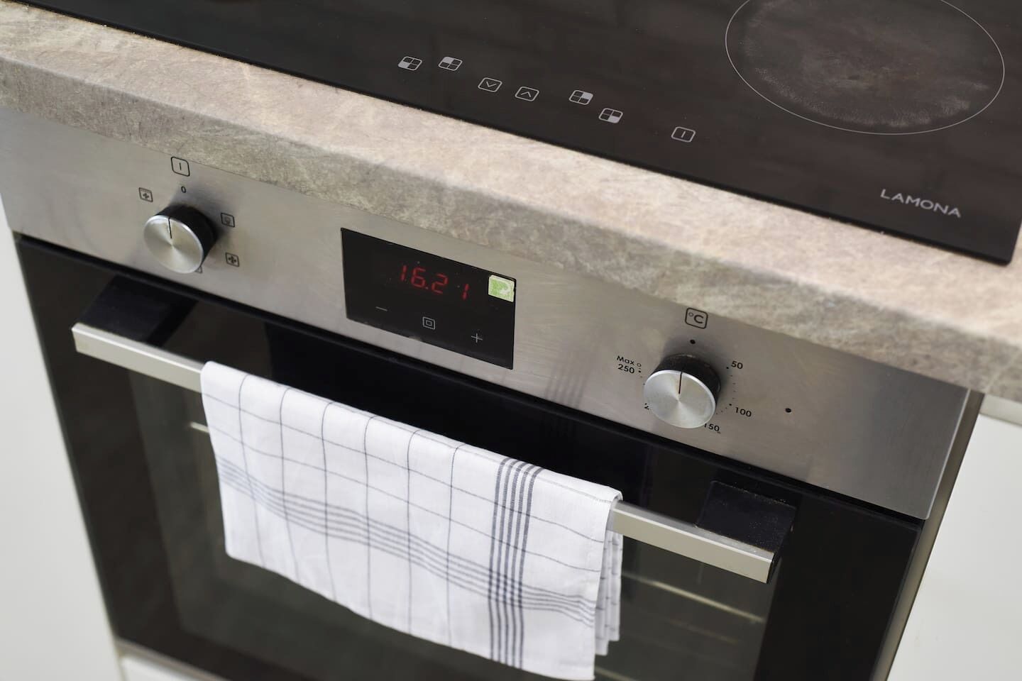 Une cuisine équipée d’un panneau de commande numérique pour le four, d’une porte de four en acier inoxydable et d’un torchon accroché à la poignée du four.