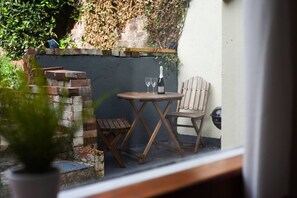 A small outdoor seating area with a table and two chairs, a bottle of wine, and a potted plant. - Clarence Cottage | 4mins to Pier, Pet Friendly with Shared Garden (Portsmouth)