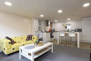 A compact living space with a sofa, a coffee table, a kitchen area with a microwave and sink, and a bar stool. - Clarence Cottage | 4mins to Pier, Pet Friendly with Shared Garden (Portsmouth)