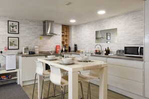 A modern kitchen with a white island, bar stools, a coffee machine, and a microwave. - Clarence Cottage | 4mins to Pier, Pet Friendly with Shared Garden (Portsmouth)