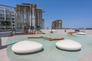 Ein Spielplatz mit weichen Bodenbelägen und Holzkonstruktionen, umgeben von modernen Gebäuden.