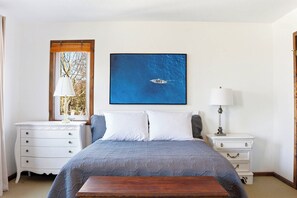 Un dormitorio con cama, dos mesitas de noche, una ventana con vistas y un cuadro en la pared.