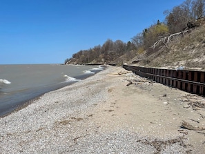 Una playa pedregosa con una valla de madera y árboles al fondo.
