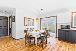 Un coin repas avec une table et des chaises en bois, un luminaire suspendu et une vue dégagée sur l’extérieur grâce à une grande fenêtre.