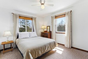 Une chambre à coucher avec un lit, une table de chevet, une lampe, une commode et des rideaux.