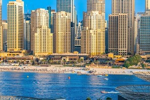 Un paysage urbain côtier avec de hauts immeubles, une plage où se trouvent des gens et des bateaux sur l’eau.