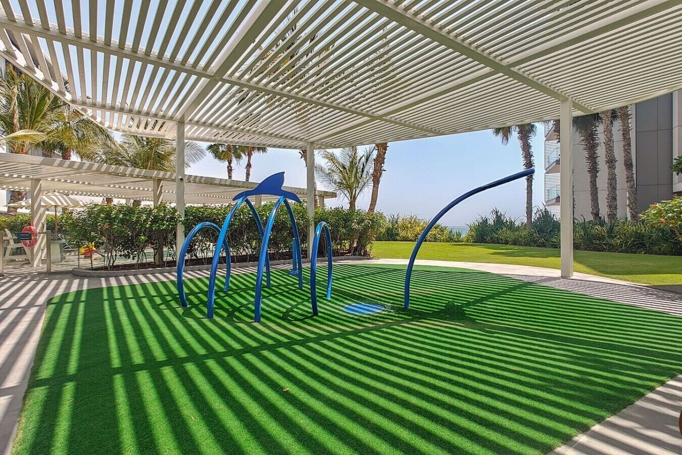 A covered outdoor area with artificial grass, a white pergola, and blue curved structures.