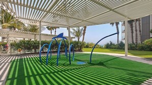 A covered outdoor area with artificial grass, a white pergola, and blue curved structures. - Vogue, Bluewater Island steps away from Ain Dubai (Bluewaters Island)
