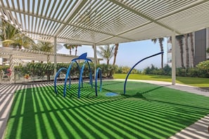 A covered outdoor area with artificial grass, a white pergola, and blue curved structures. - Vogue, Bluewater Island steps away from Ain Dubai (Bluewaters Island)