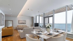 Un salon moderne avec un canapé, une table à manger pour quatre personnes et de grandes fenêtres offrant une vue sur la mer.