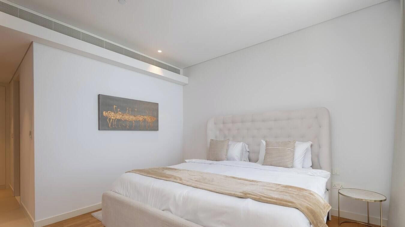 A bedroom with a large bed, a headboard, a small round table, and a painting on the wall.