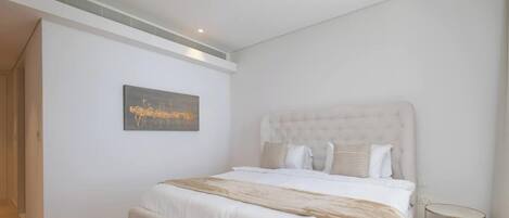 A bedroom with a large bed, a headboard, a small round table, and a painting on the wall.
