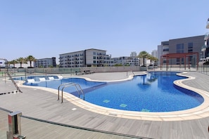 Ein Pool mit wellenförmigem Rand, umgeben von einer Holzterrasse und einem Glasgeländer.