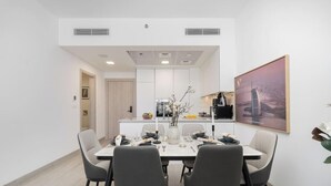 Ein moderner Essbereich mit einem weißen Tisch, gedeckt für vier Personen, einer Küche im Hintergrund und einem großen gerahmten Bild an der Wand.