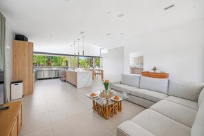 A modern kitchen with a central island, a dining area with a glass table, and a living area with a sofa.