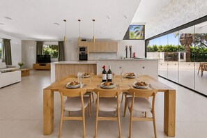 A modern kitchen with wooden cabinets, a dining table set for four, and a large window overlooking a garden.
