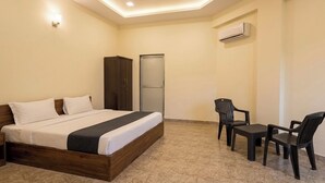 Een slaapkamer met een bed, een kledingkast, een bureau, twee stoelen en een airconditioning.