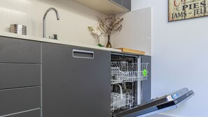 Ett modernt kök med en inbyggd diskmaskin, en kran i rostfritt stål och en vas med torkade blommor på bänkskivan.