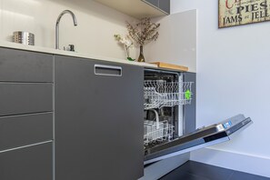 Una cocina moderna con lavavajillas integrado, un grifo de acero inoxidable y un florero con flores secas sobre la encimera.