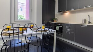 Ett modernt kök med mörka skåp, en vit bänkskiva och en matplats med ett bord dukat för två personer.