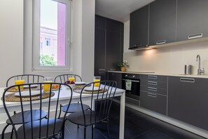 Una cocina moderna con armarios oscuros, una encimera blanca y una zona de comedor con una mesa preparada para dos personas.
