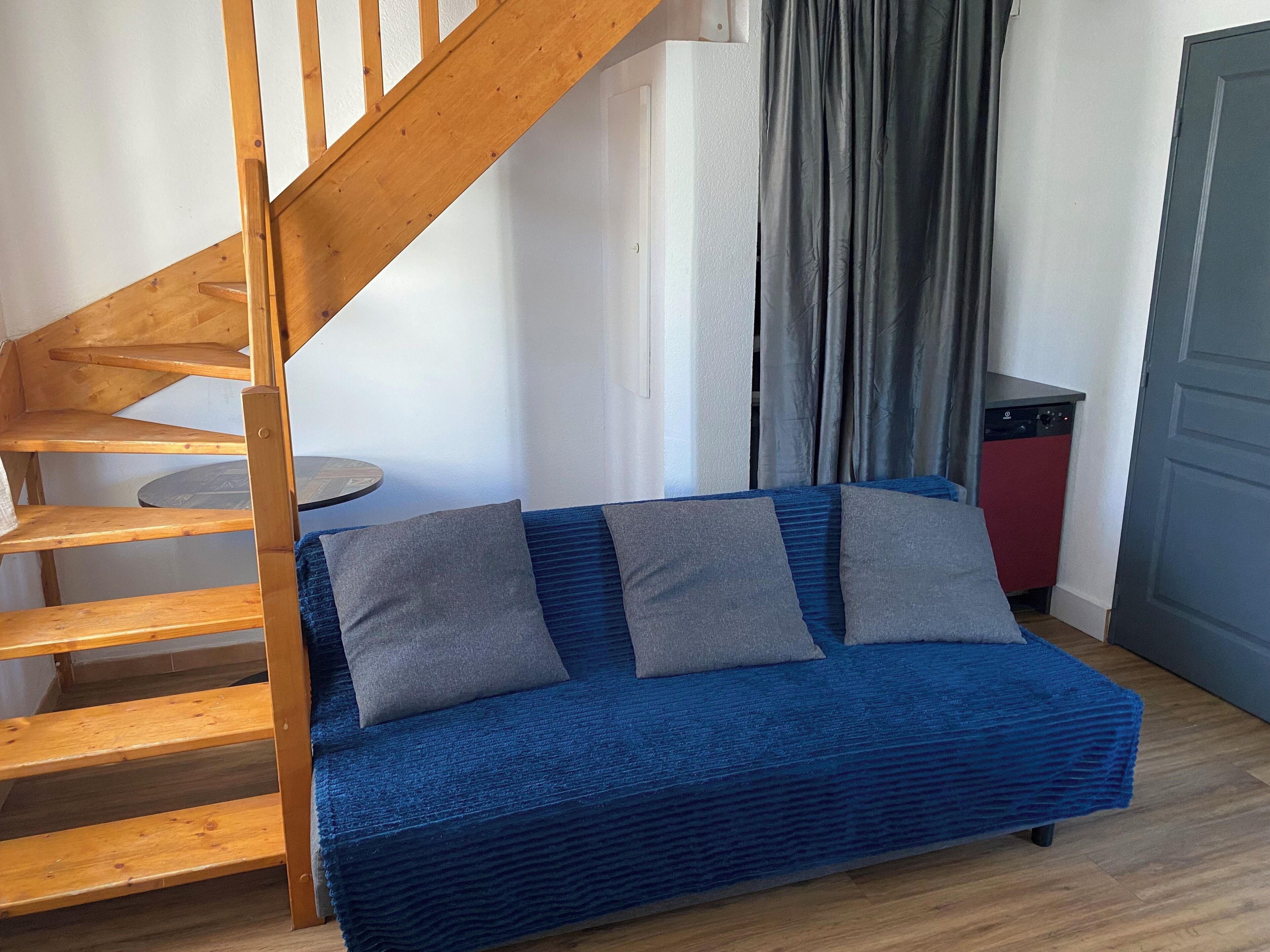 Une pièce avec un canapé bleu, un escalier en bois et un appareil électroménager rouge.