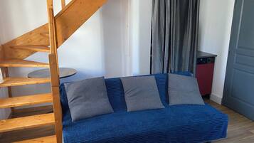 Une pièce avec un canapé bleu, un escalier en bois et un appareil électroménager rouge.
