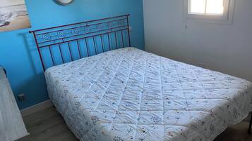 Une pièce avec un lit, une lampe fixée au mur et une fenêtre.