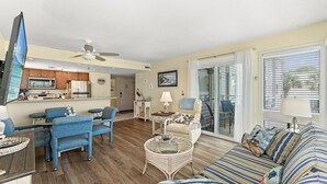 A living room with a sofa, chairs, a small table, and a television. - Coastal Getaway Arcadian Dunes #250 -Steps to Sand (Myrtle Beach)