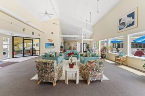 Eine großzügige Lobby mit türkisfarbenen Sofas, einem zentralen weißen Tisch und großen Fenstern mit blauen Sonnenschirmen.