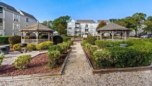 A courtyard with two gazebos, a gravel path, and a garden with trimmed bushes. - Coastal Getaway Arcadian Dunes #250 -Steps to Sand (Myrtle Beach)